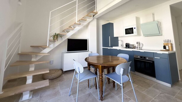 A modern kitchen with a dining area, a staircase, and a flat-screen TV.