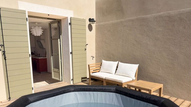 Un jacuzzi con cubierta de madera, un sofá con cojines y una cocina visible a través de una puerta abierta.