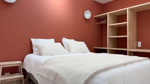 Un dormitorio con cama, mesitas de noche, un armario y una pequeña estantería.