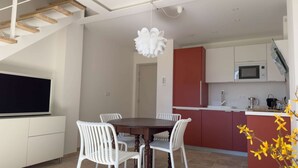 Una cocina moderna con zona de comedor, que incluye una escalera de madera, sillas blancas y una isla central.