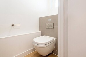 A small, modern bathroom with a white toilet, a shower area, and a wall-mounted control panel.