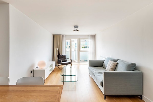 Una sala de estar moderna con una mesa de centro de vidrio, un sofá gris y una silla negra.