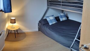 Un dormitorio compacto con literas, una mesita de noche con lámpara y un cojín azul a cuadros.