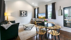 Una sala de estar moderna con sofá, una mesa de comedor con sillas, televisión y un ventanal grande.