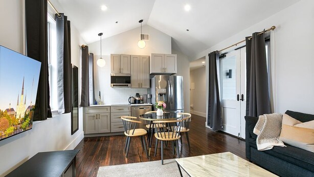 Una cocina moderna con electrodomésticos de acero inoxidable, un comedor con una mesa redonda y sillas, y una sala de estar con un sofá y televisor.