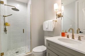A modern bathroom with a glass-enclosed shower, a white toilet, a vanity with a sink, and a mirror. - 2BR/2BA Retreat at The Heart of New Orleans (New Orleans)