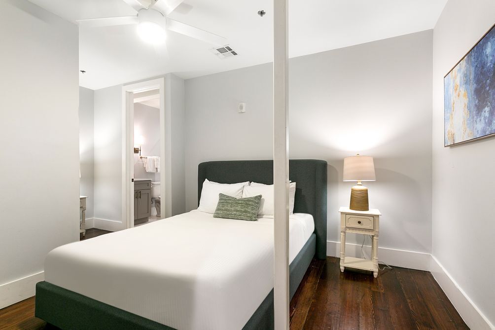 Quarto com uma cama, mesa de cabeceira, abajur e um quadro na parede.