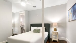 Un dormitorio con cama, mesita de noche, lámpara y un cuadro en la pared.