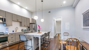 A modern kitchen with a central island, stainless steel appliances, and a dining area with a glass table and wooden chairs. - Luxurious 5bd with private balcony/ AMAZING LOCATION! (New Orleans)