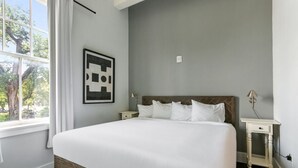 Quarto com cama grande, mesa de cabeceira, quadro na parede e janela com cortinas.