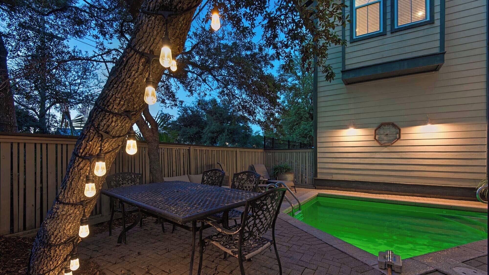 En udendørs terrasse med et metalbord og stole, omgivet af et træhegn og et træ.