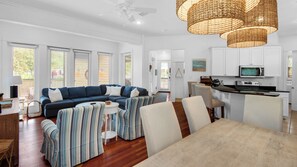 A spacious living room with a blue sofa, striped armchairs, a dining table, and a kitchen area with white cabinets and appliances.