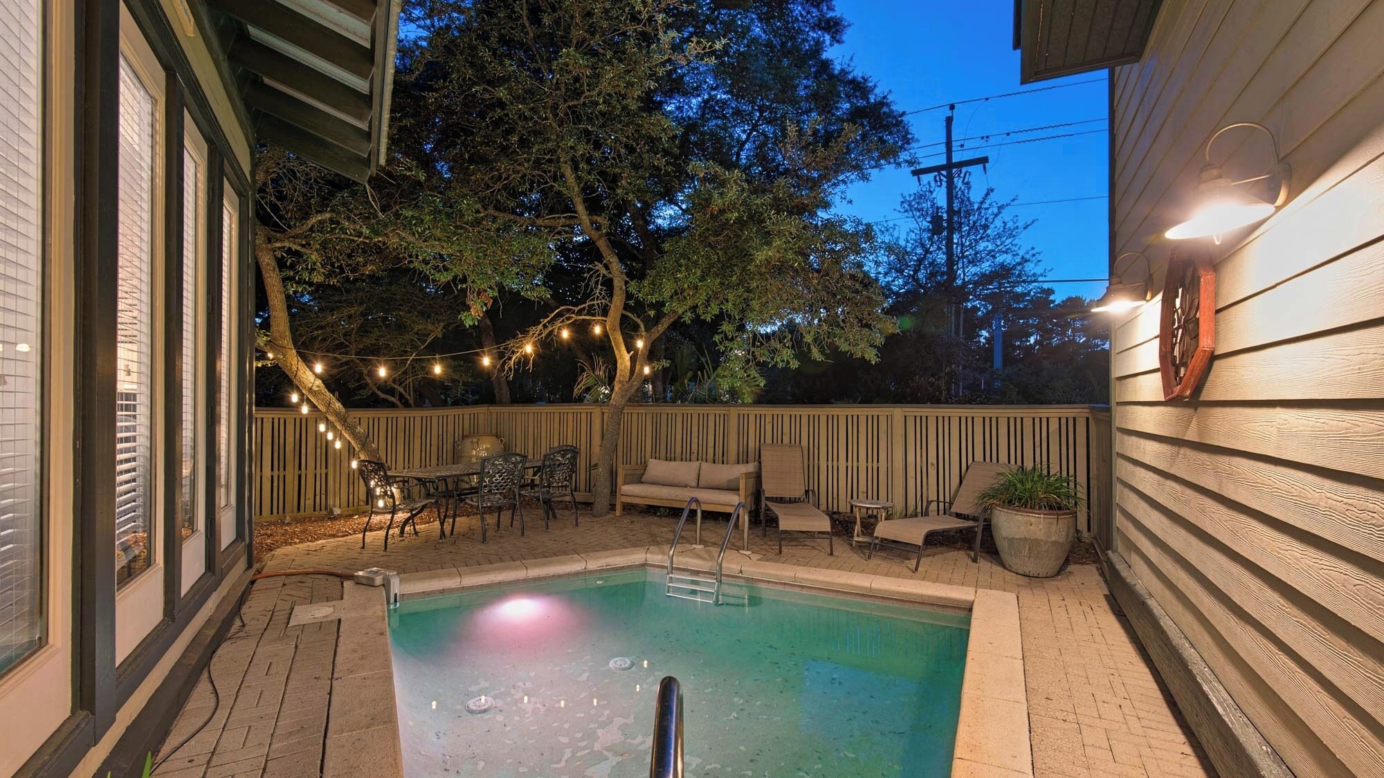 A backyard with a swimming pool, patio furniture, and string lights.
