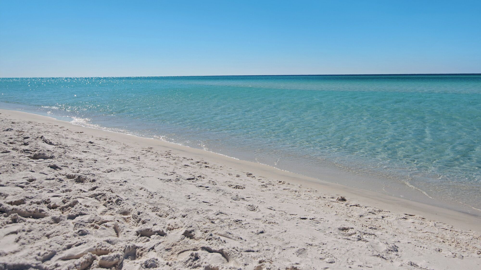 Une plage de sable fin, avec une eau turquoise et limpide et un ciel dégagé.