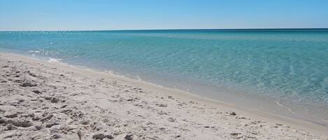 Une plage de sable fin, avec une eau turquoise et limpide et un ciel dégagé.