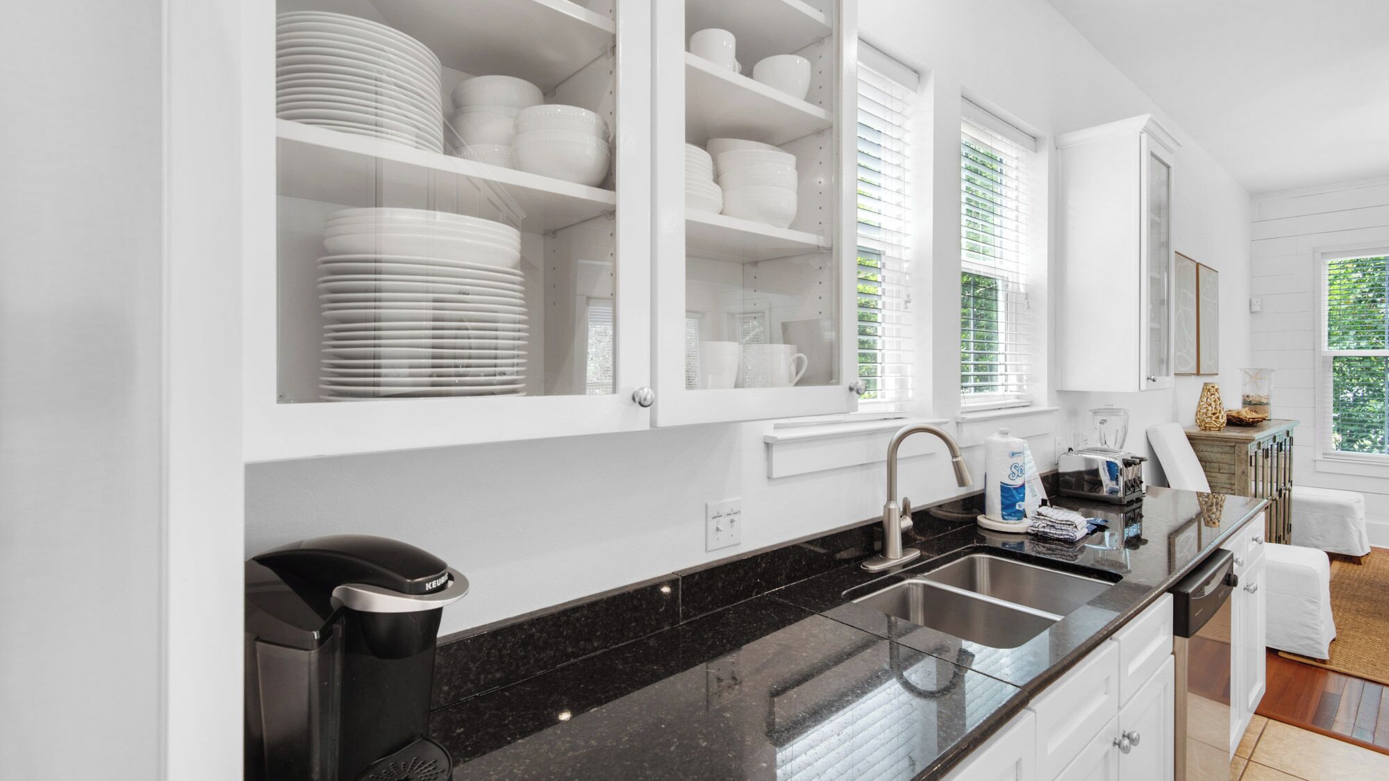 A modern kitchen with white cabinetry, a black granite countertop, and a stainless steel sink.