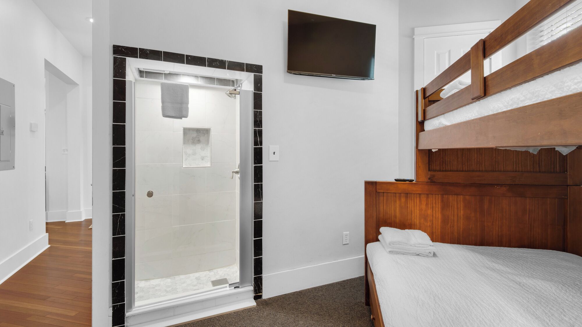 A bedroom with a shower, a TV mounted on the wall, and a bunk bed.