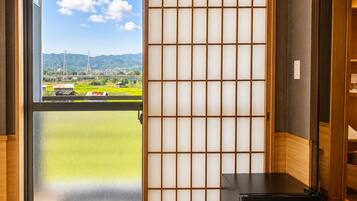 Habitación con puerta corredera estilo shoji, un refrigerador negro y vista a un paisaje verde con montañas.