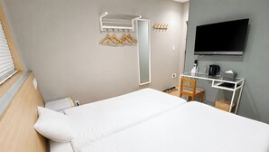 A hotel room with a bed, a TV, a desk with a chair, and a coat rack.