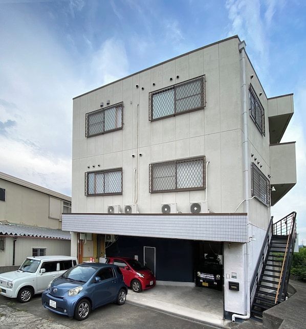A multi-story building with a garage entrance, parked cars, and a staircase leading to an upper level. - My Home Inn Sennan Onosato (Sennan)