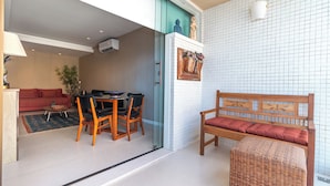 Una sala de estar moderna con comedor, un sofá, un banco de mimbre y un estante de pared con objetos decorativos.