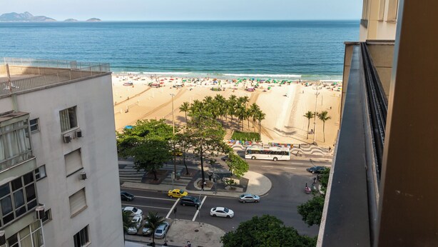 Vista de la playa desde un edificio alto, con una imagen despejada de la playa, palmeras y una carretera con coches y un autobús.