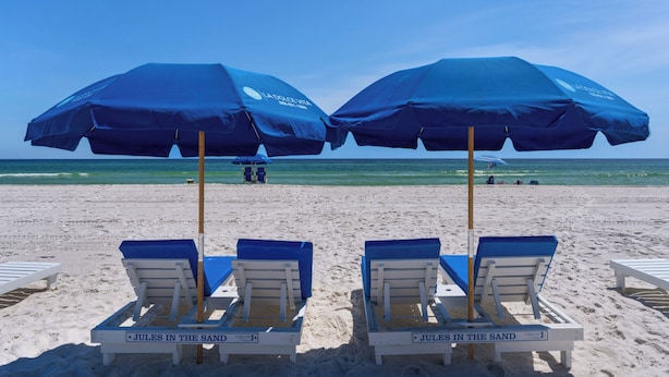 Une plage avec deux parasols bleus, des chaises longues et un panneau indiquant : « Jules sur le sable ».