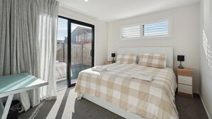 Un dormitorio con cama, mesita de noche, escritorio y puerta corrediza de vidrio que da a un balcón.