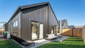 Una casa moderna con un gran ventanal corredera que da a un patio con un sofá y una mesa.