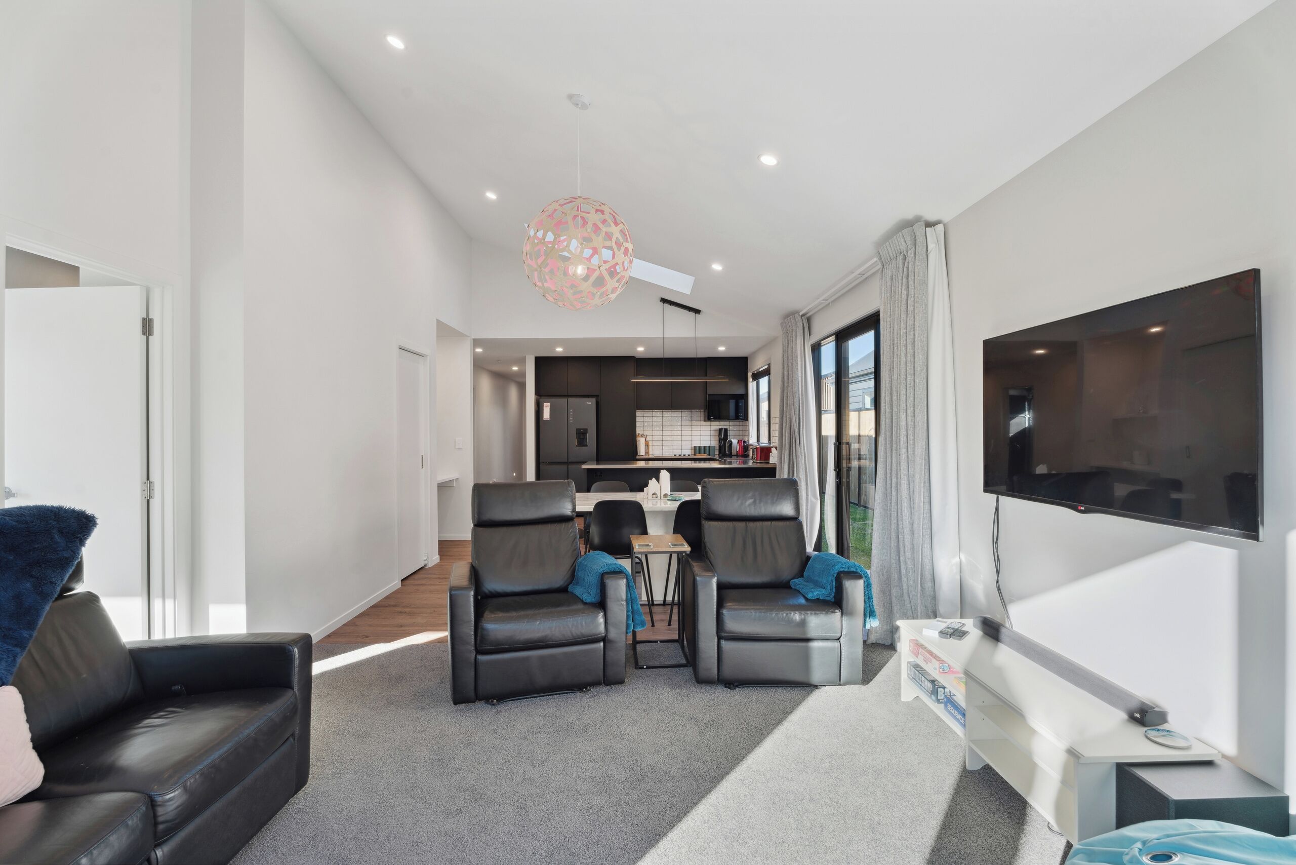 Un salon moderne avec un canapé, deux fauteuils, un téléviseur et une cuisine en arrière-plan.
