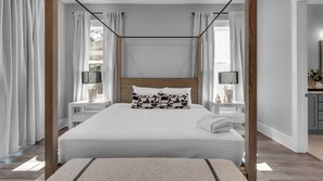 Ein modernes Schlafzimmer mit Baldachinbett, weißer Bettwäsche und einem Nachttisch mit Lampe.