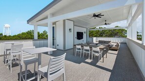 Eine Terrasse im Freien mit weißer Möbel, einem Deckenventilator und Blick zum Himmel.