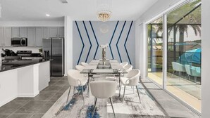 A modern kitchen with white cabinets, stainless steel appliances, and a dining area with a glass table and white chairs. - *NEW* Super Amazing Vacation Getaway (Kissimmee)