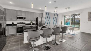 A modern kitchen with grey cabinets, stainless steel appliances, and a central island with bar stools. - *NEW* Super Amazing Vacation Getaway (Kissimmee)