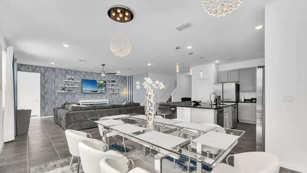 A modern living room with a glass dining table, white chairs, a grey sofa, and a TV on the wall. - *NEW* Super Amazing Vacation Getaway (Kissimmee)