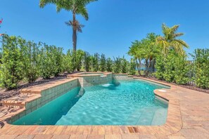 Una piscina con borde de azulejos, rodeada por un jardín ajardinado con palmeras y arbustos.