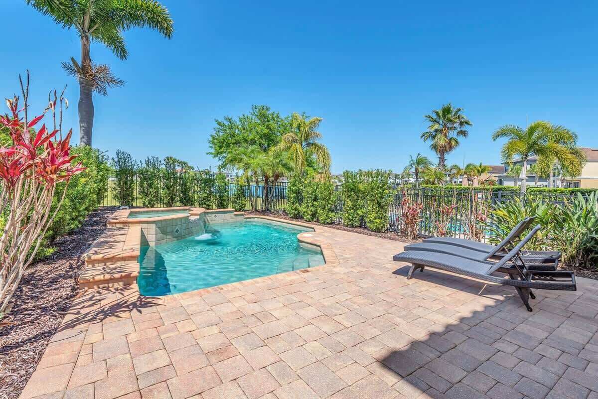 Une piscine rectangulaire, bordée d’un sol carrelé et entourée de palmiers et d’autres plantes.