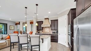 A modern kitchen with a central island, dark cabinetry, and a stainless steel refrigerator. - Main Street USA in Luxury Reunion Home (Reunion)