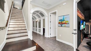 A spacious hallway with a wooden staircase, white arches, and a modern art piece on the wall. - Main Street USA in Luxury Reunion Home (Reunion)