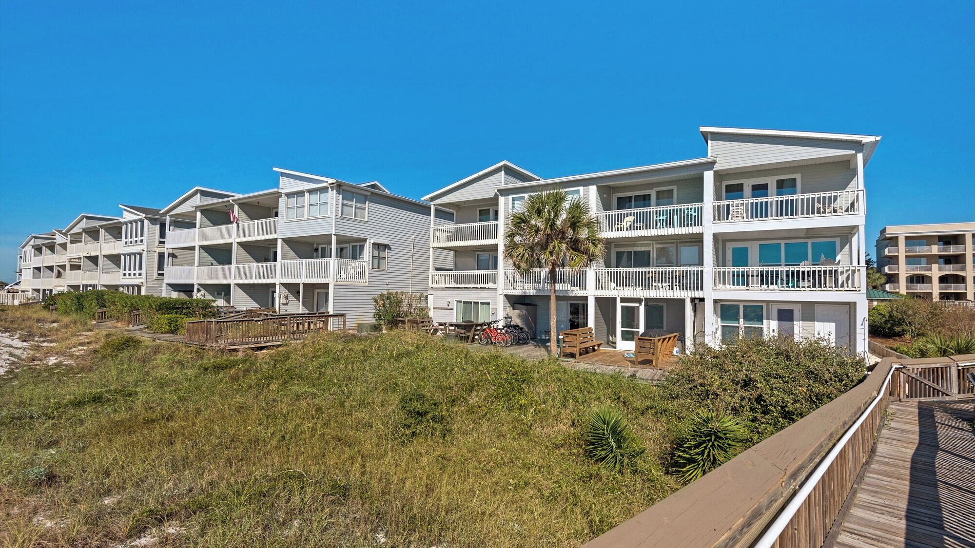 A beachfront hotel with multiple balconies, a wooden boardwalk, and a palm tree.