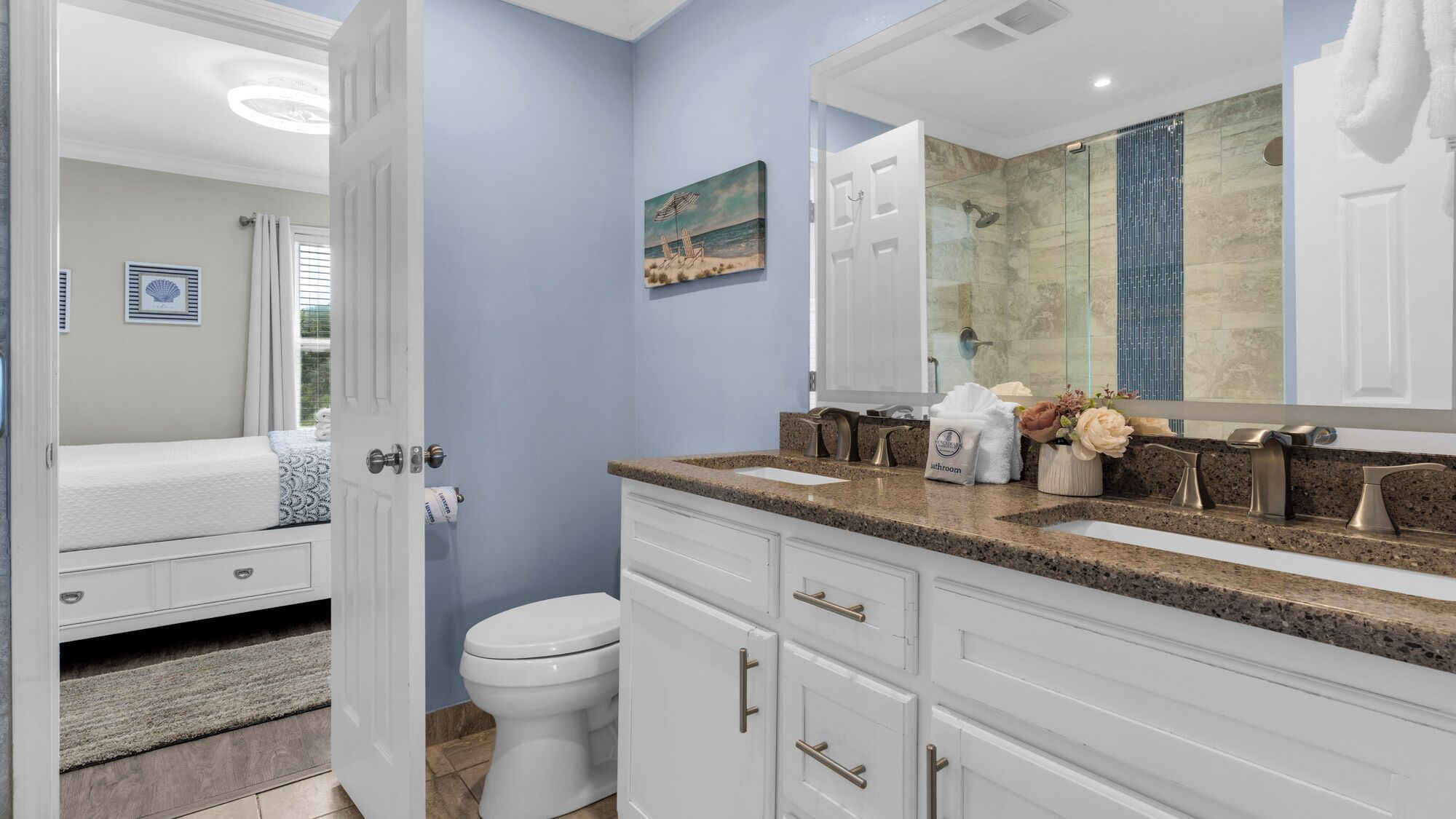 A bathroom with a white toilet, a sink with a granite countertop, and a large mirror above the sink.