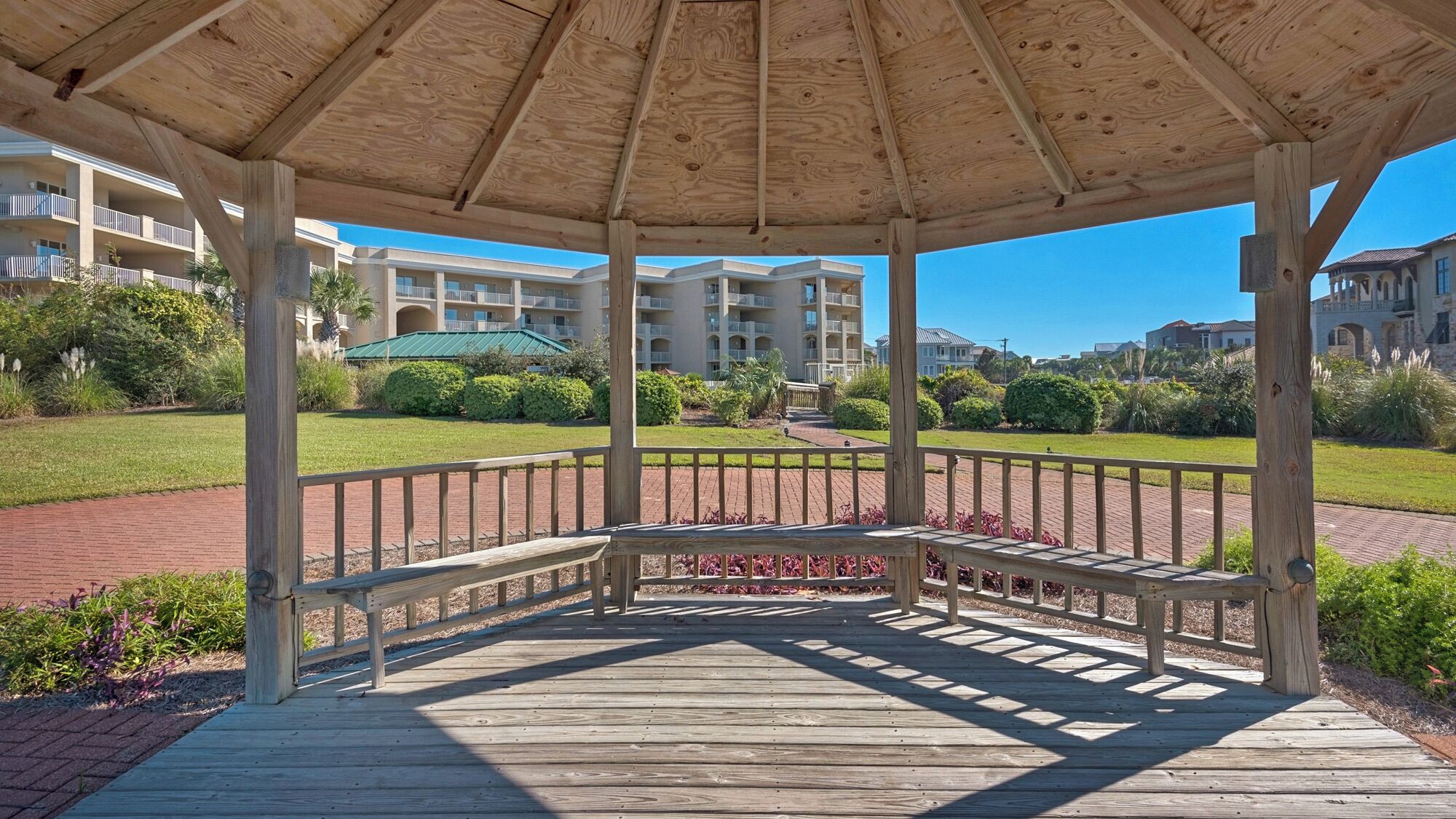 A wooden gazebo with a brick pathway leading to a building complex.