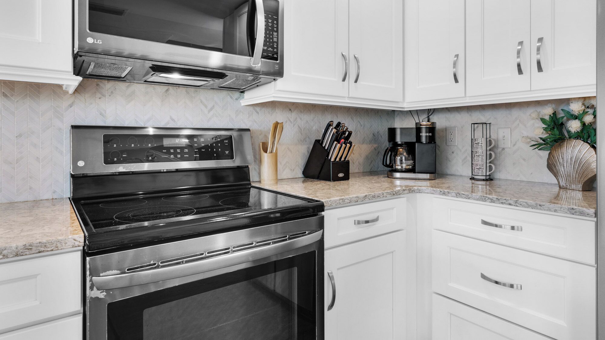 Una cocina moderna con armarios blancos, un microondas de acero inoxidable, un horno y una cafetera.