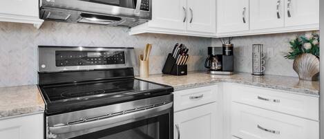 Una cocina moderna con armarios blancos, un microondas de acero inoxidable, un horno y una cafetera.