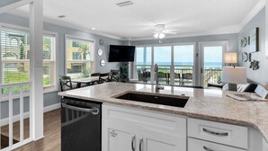 A modern kitchen with a large island, a built-in dishwasher, and a view of the ocean through large windows. - Modern & Updated - Gulf-front - Steps to the Beach (Santa Rosa Beach)