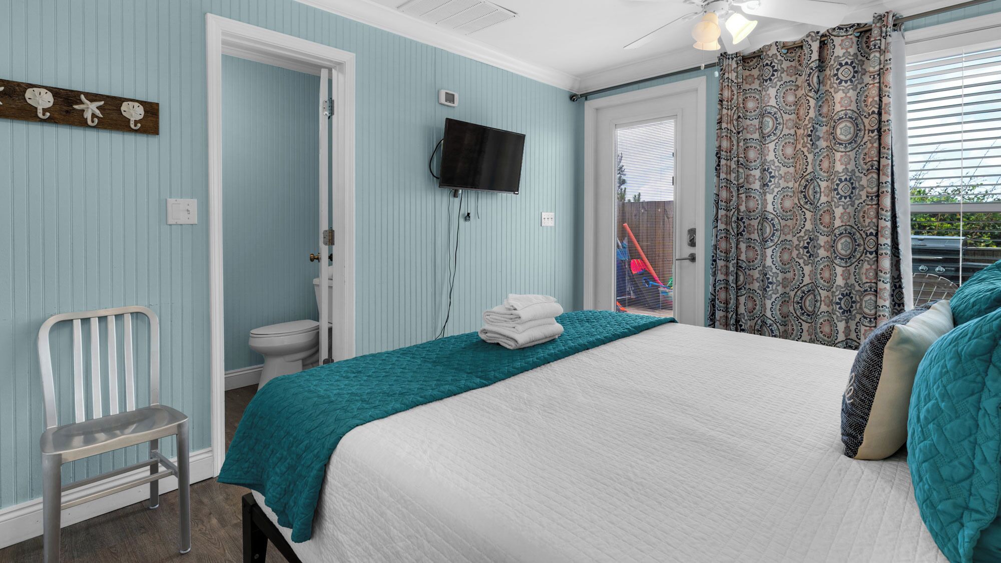 A bedroom with a bed, a chair, a toilet, and a TV.