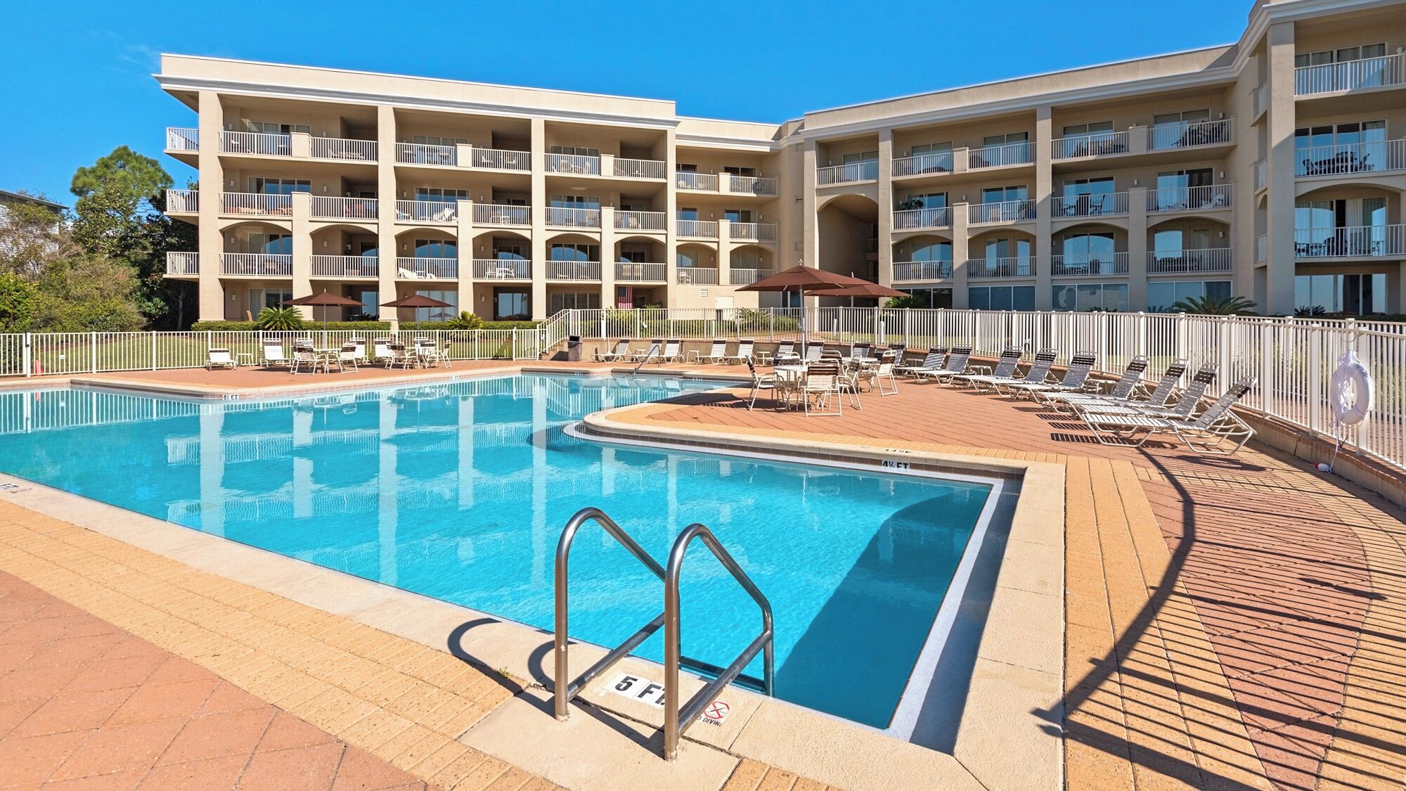 A swimming pool with sun loungers and a building with multiple balconies in the background.