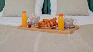 A neatly made bed with a green upholstered headboard, two pillows, a tray with croissants, orange juice, and a glass of water. - 397 Suite Glamour - Superb Studio in Paris (Paris 10 Entrepôt)