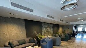 Un hall d’entrée moderne avec un sol en marbre, des canapés gris et une table basse ronde.