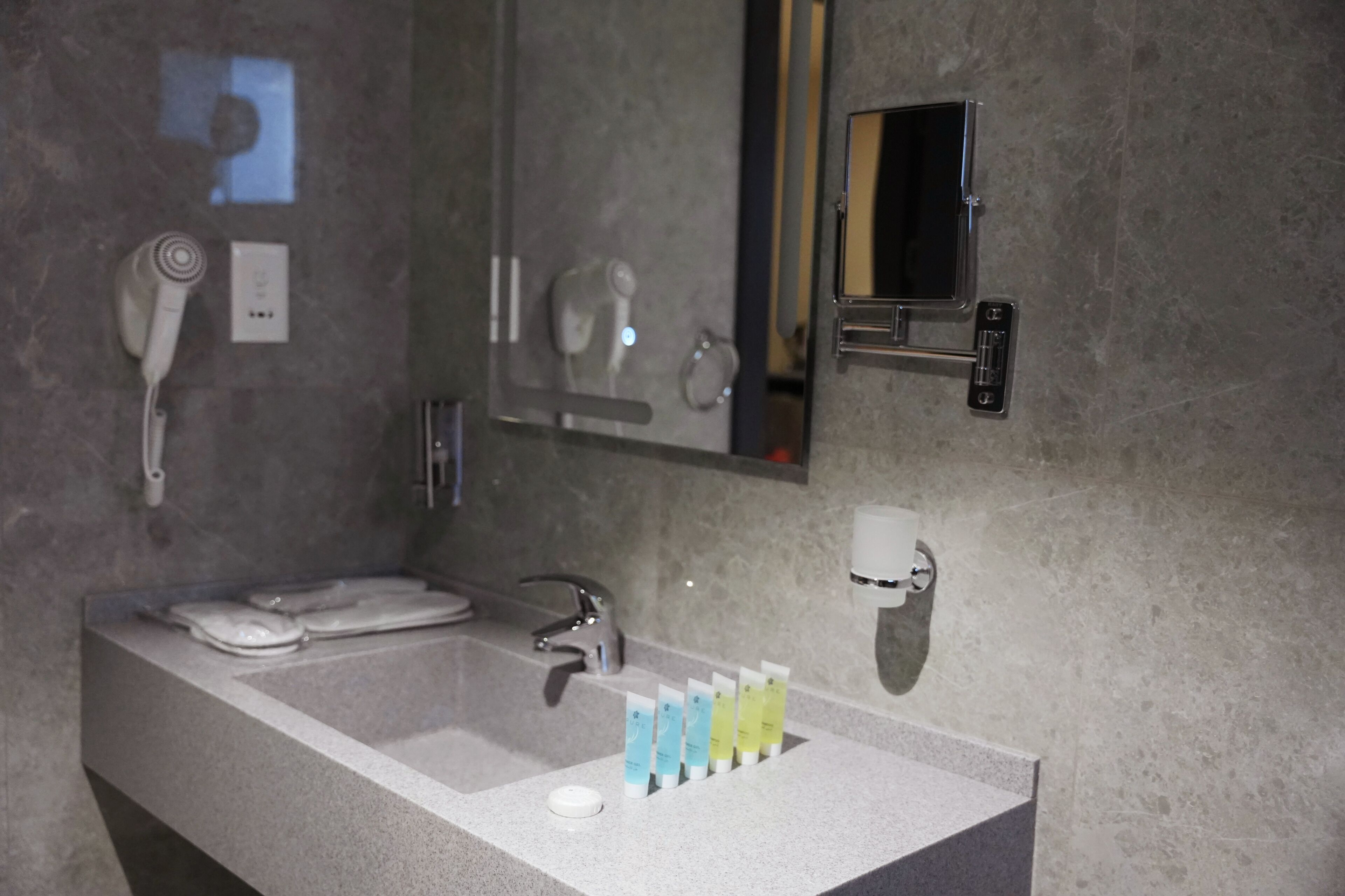 Un baño moderno con un lavamanos grande, un secador de pelo de mano, un espejo y un set de artículos de aseo.